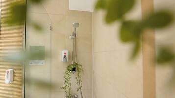 A bathroom with a shower, a hand soap dispenser, and a potted plant.