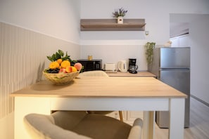 Une cuisine moderne avec une table en bois, un panier de fruits, une machine à café et un réfrigérateur.