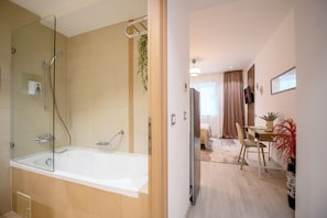 A modern bathroom with a glass-enclosed shower, a white bathtub, and a wooden floor. - Gateway to Modern Elegance (Bucharest)