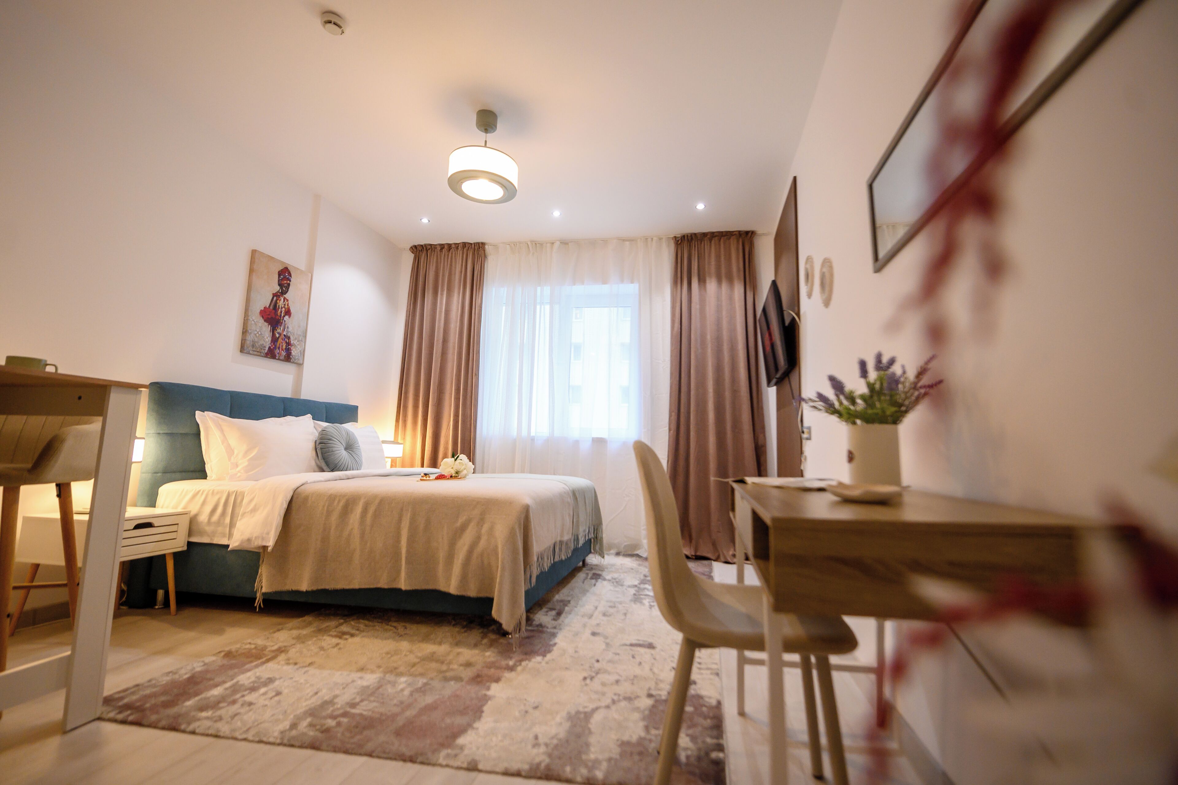 Un dormitorio con cama, mesita de noche, silla, escritorio y ventana con cortinas.