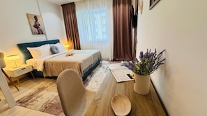 Ein Hotelzimmer mit Bett, Schreibtisch, Stuhl, einer Topfpflanze und einem an der Wand befestigten Fernseher.