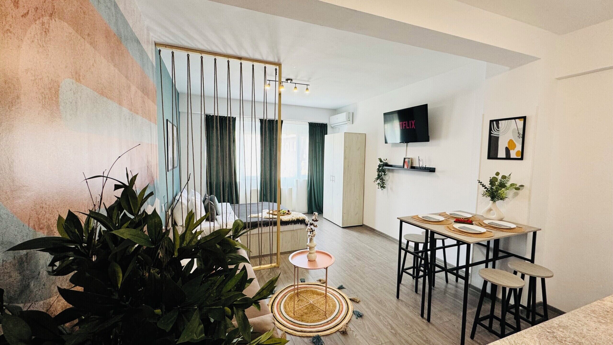 A modern living room with a dining area, a TV mounted on the wall, and a staircase leading to another level.