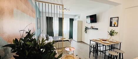 A modern living room with a dining area, a TV mounted on the wall, and a staircase leading to another level.