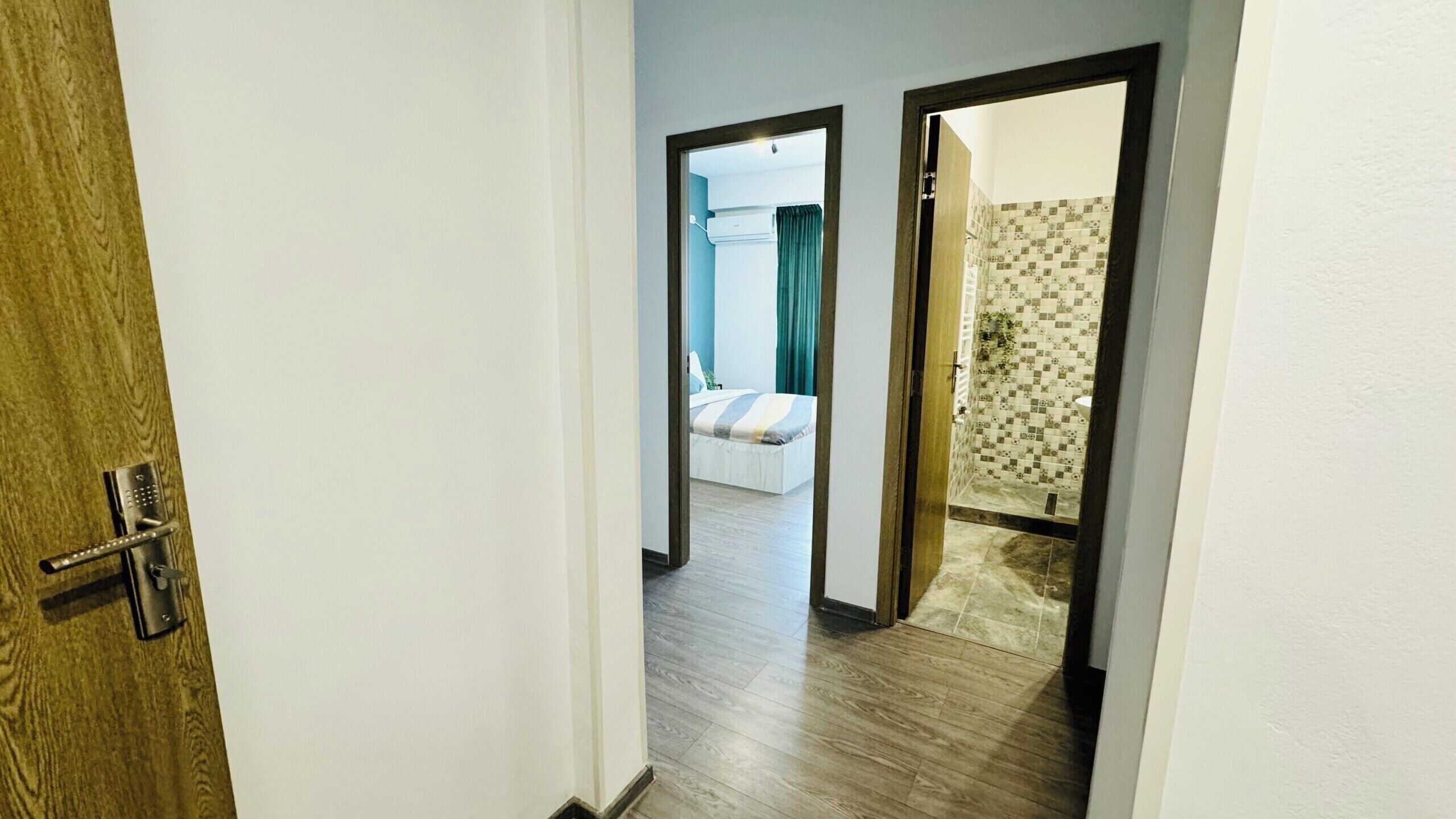 Een gang die leidt naar een slaapkamer met een bed, een badkamer met een mozaïek van tegels, en een deur met een sleutel slot.