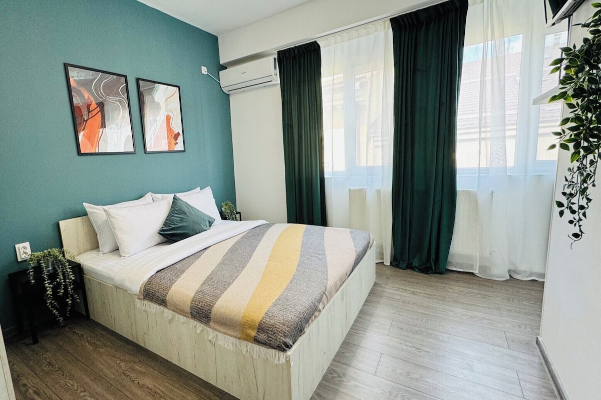 A bedroom with a bed, a wall-mounted air conditioner, and a window with curtains.