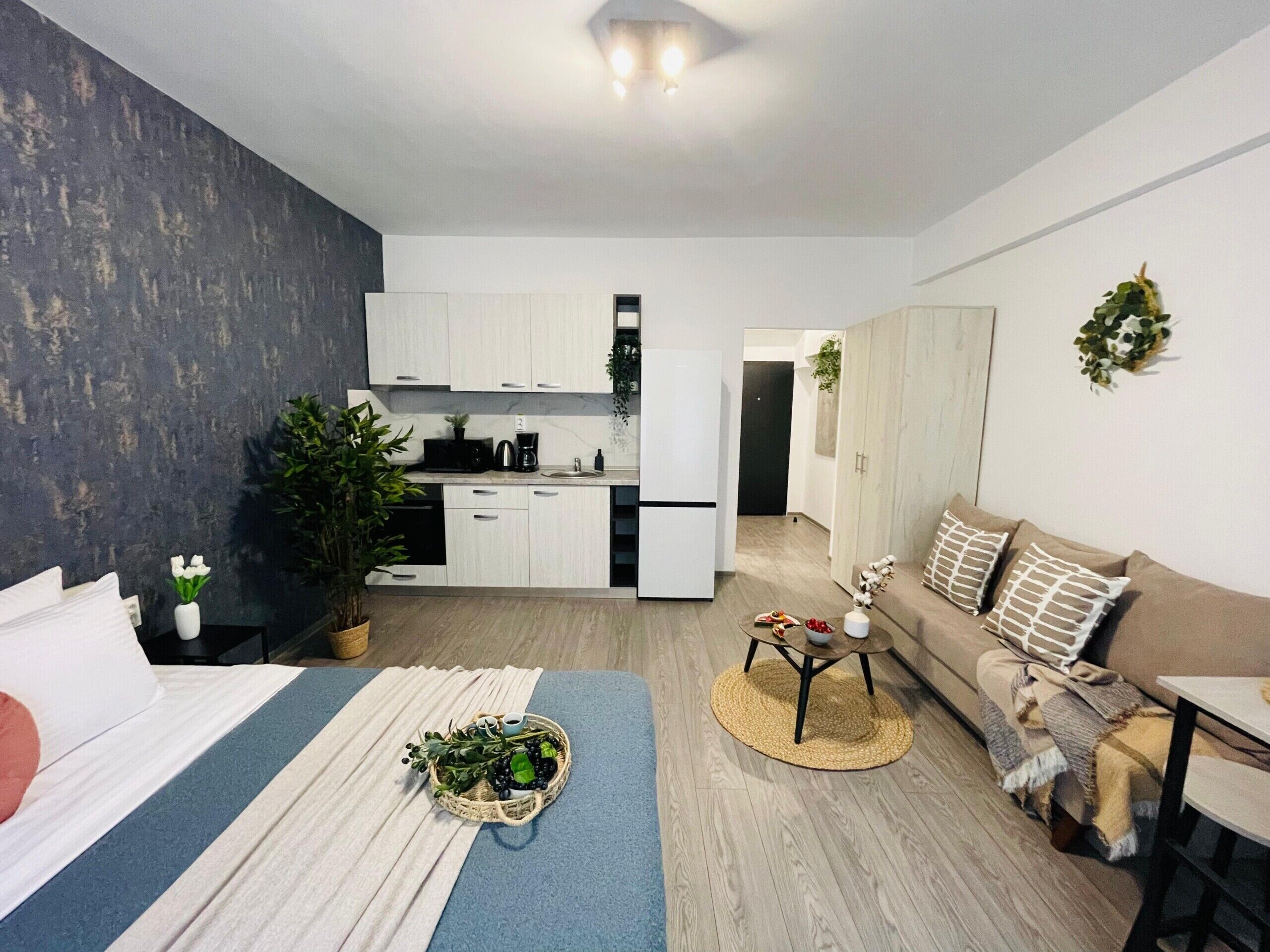 A modern apartment with a kitchenette, a dining area, a living room with a sofa and coffee table, and a bed with a blue and white striped bedspread.