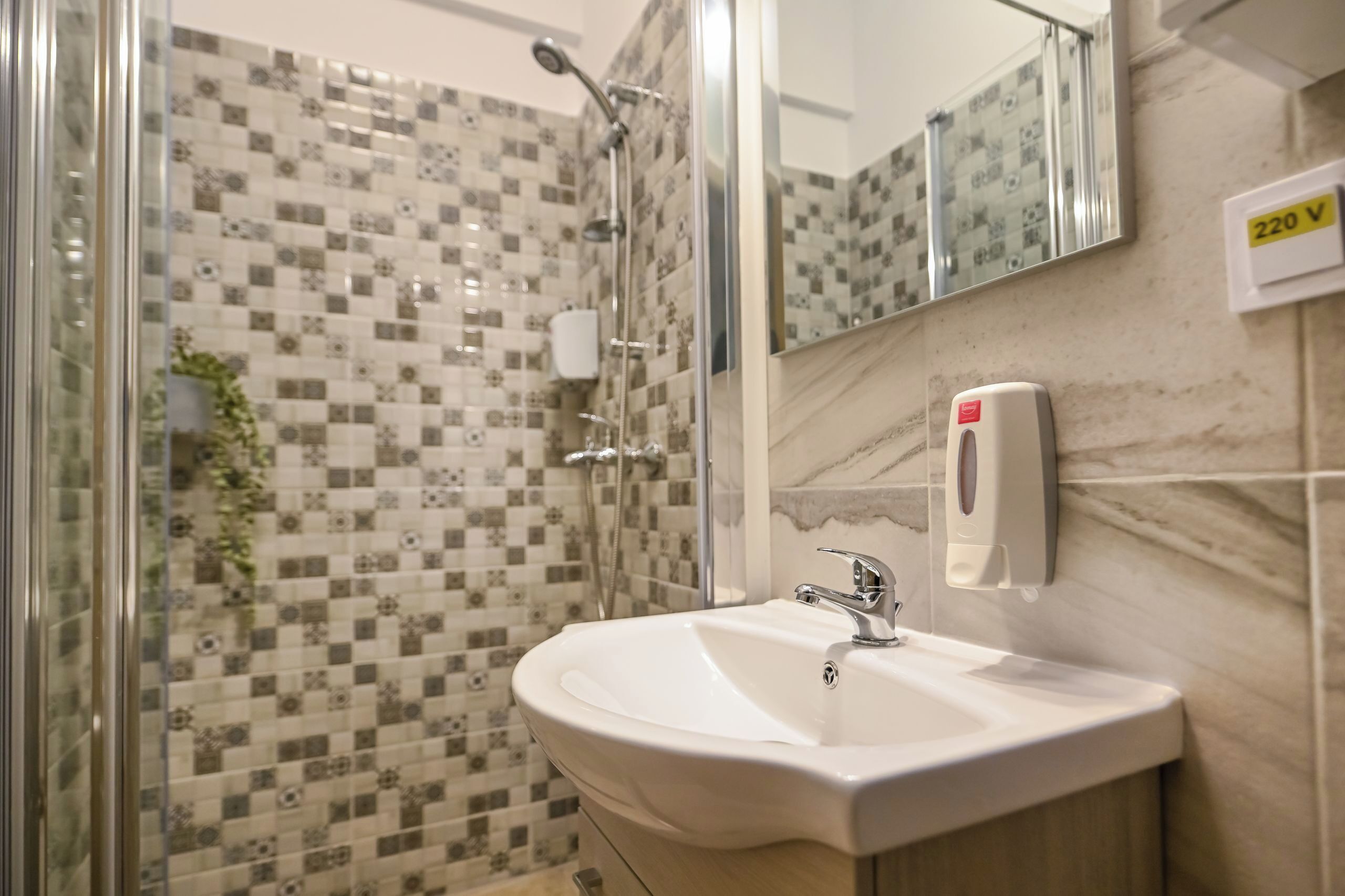 A bathroom with a shower, a sink, a mirror, and a hand sanitizer dispenser.