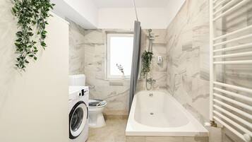 A bathroom with a washing machine, toilet, and bathtub.