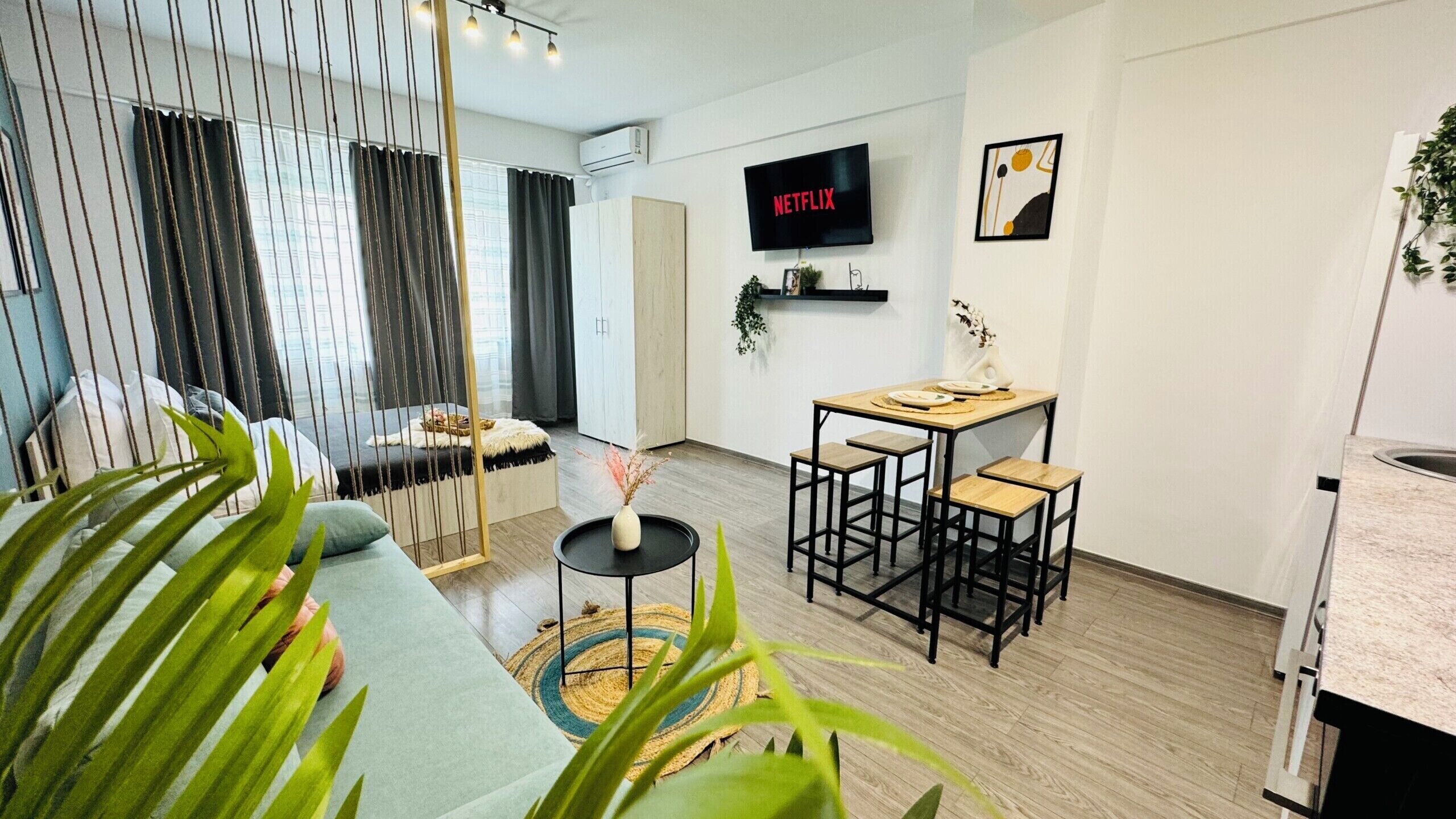 Ein modernes Wohnzimmer mit einer Couch, einem Essbereich mit Tisch und Stühlen, einem an der Wand befestigten Fernseher und einer Küchenzeile.