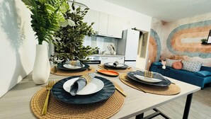 A modern kitchen with white cabinets, a dining table set with plates and cutlery, and a large green plant. - Modern Apartments in the Heart of the City (Bucharest)