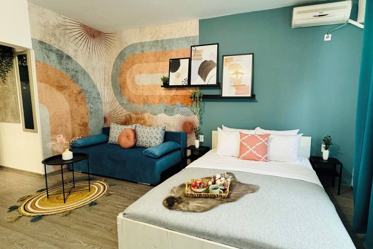 A modern bedroom with a bed, a blue sofa, a small table, and a wall with abstract art.
