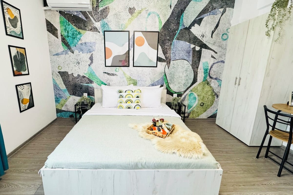 A modern bedroom with a large bed, a small round table, and a wall with abstract art.