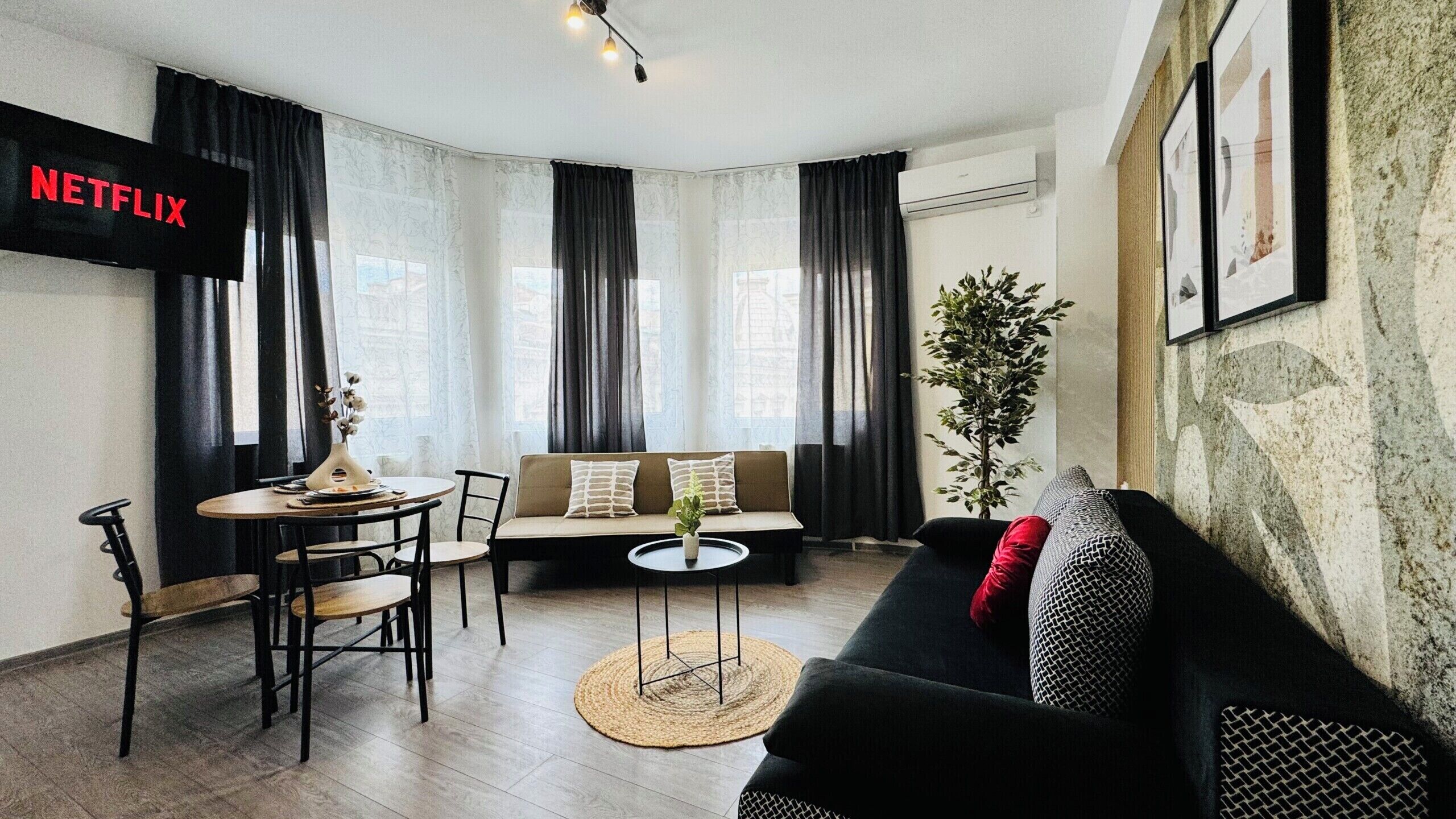 A modern living room with a sofa, a dining table, and a TV mounted on the wall.