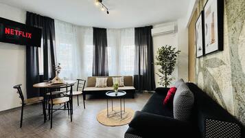 A modern living room with a sofa, a dining table, and a TV mounted on the wall.