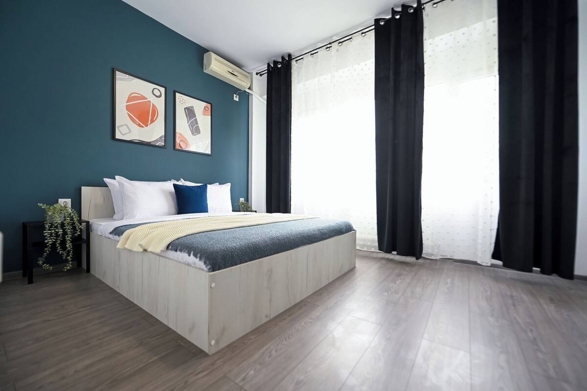 A modern bedroom with a wooden bed, a nightstand, a potted plant, and two framed pictures on the wall.