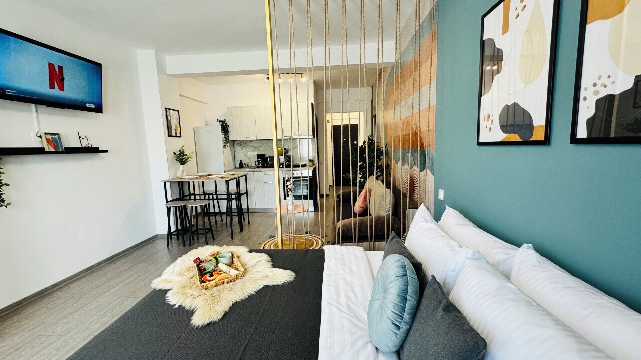 Een moderne woonkamer met een bank, een aan de muur bevestigde televisie en een eethoek met stoelen en een tafel.