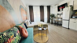 A modern apartment with a sofa, a small round table, a kitchen area, and a large window with curtains. - Modern Apartments in the Heart of the City (Bucharest)