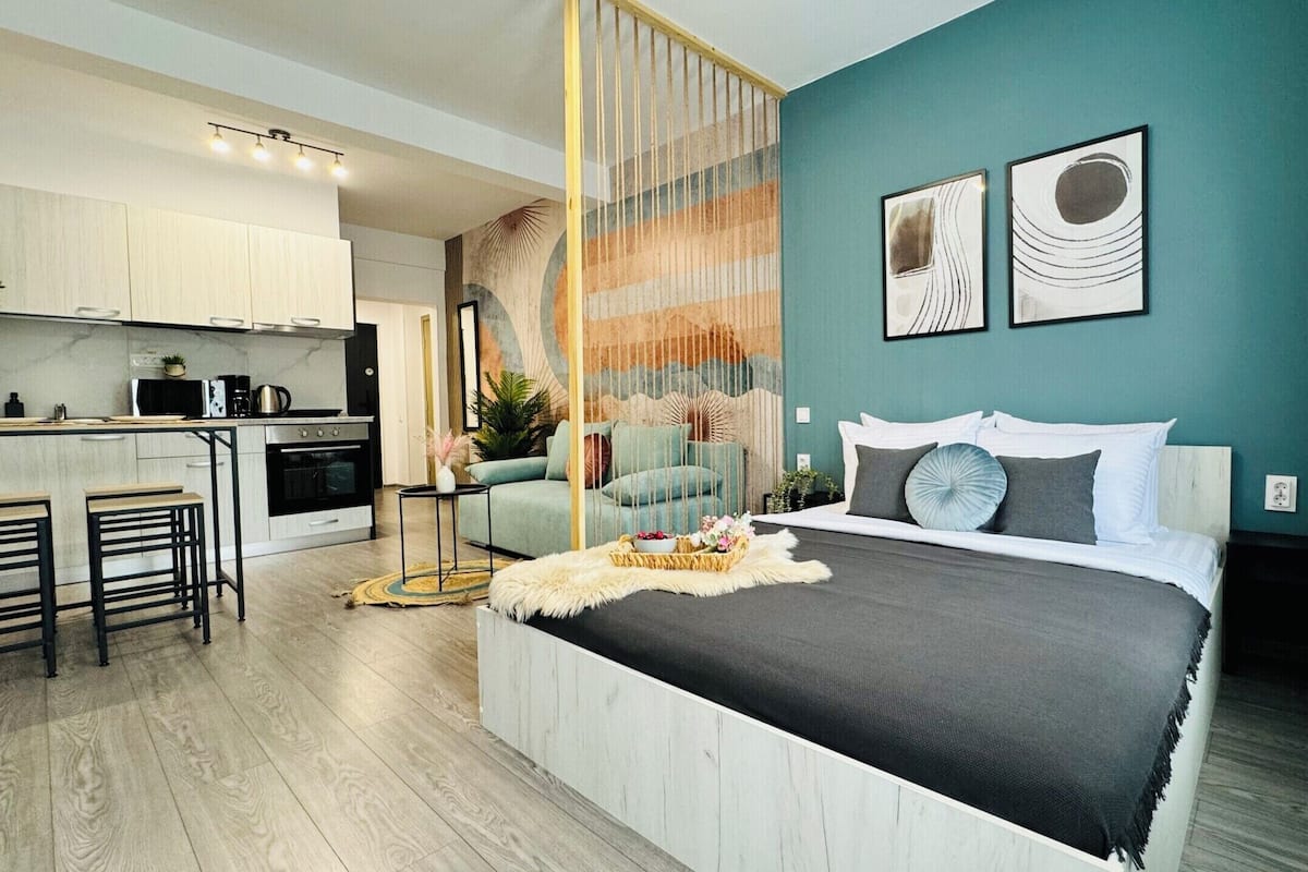 A modern bedroom with a bed, a sofa, and a kitchen area.