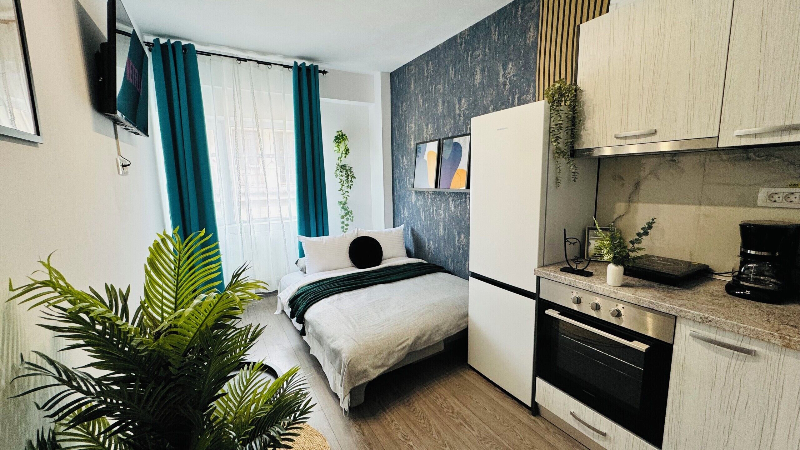 A compact bedroom with a bed, a small kitchenette, and a window with curtains.