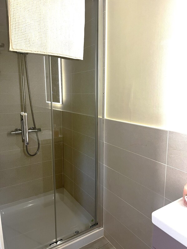 Ducha con puerta de vidrio, cabezal de ducha de mano y barra para toallas.