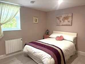 A bedroom with a bed, a radiator, a window with curtains, a bedside table with a lamp, and a world map on the wall. - Ower Retreat Rosscahill (Rosscahill)