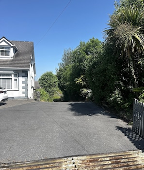 A residential driveway with a house on the left, surrounded by greenery and a palm tree. - Ower Retreat Rosscahill (Rosscahill)