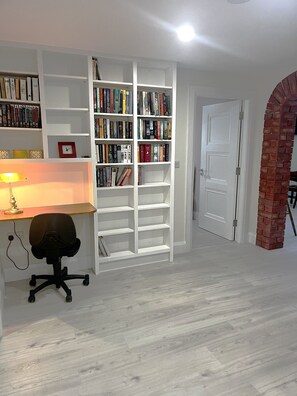 Una habitación con una estantería blanca, un escritorio con una silla y una puerta.