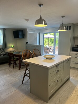 A modern kitchen with a central island, pendant lighting, and a dining area with wooden chairs. - Ower Retreat Rosscahill (Rosscahill)