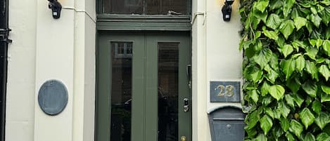 A building entrance with a green door, two wall-mounted lamps, and a sign above the door.