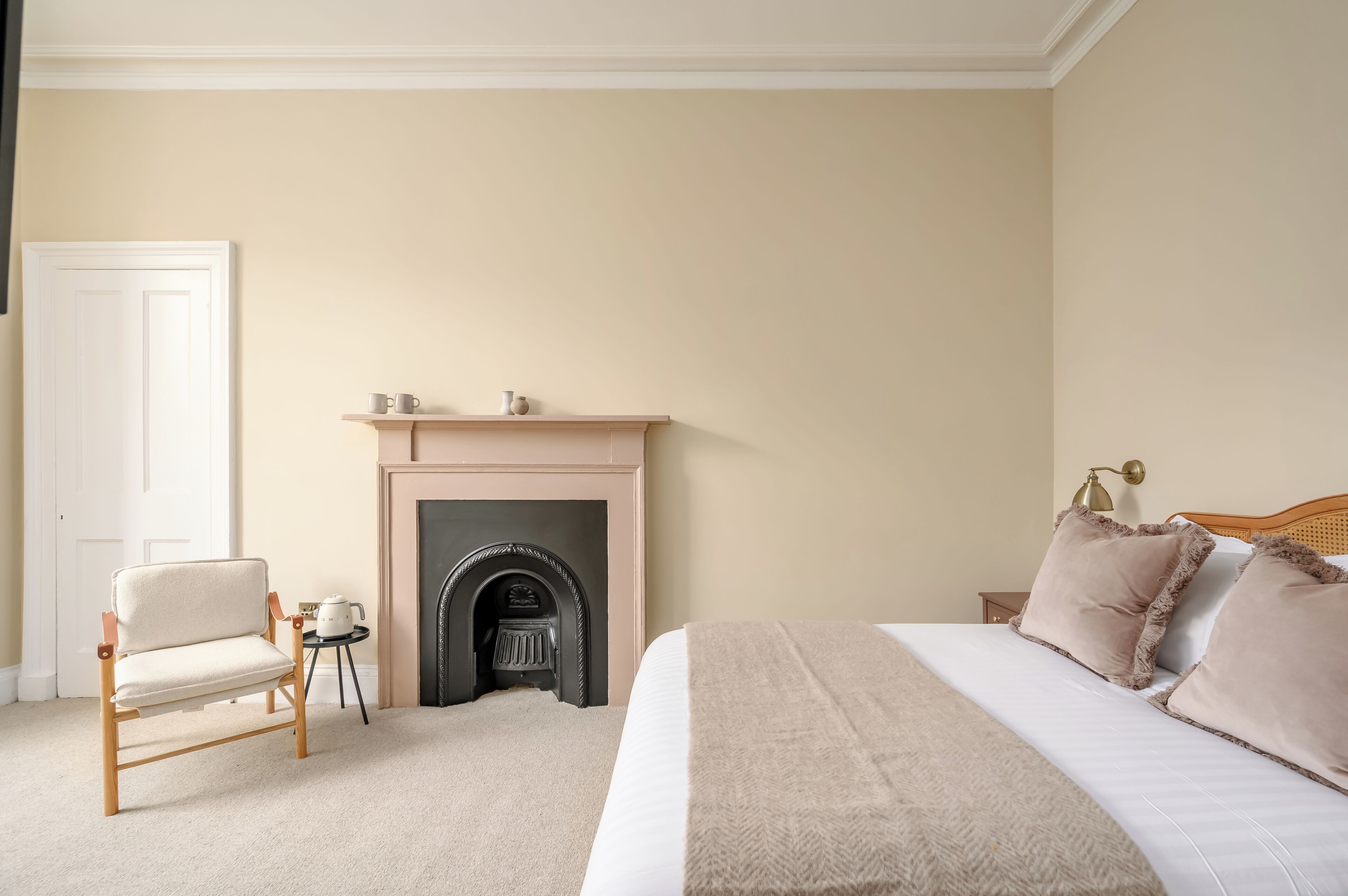 Un dormitorio con cama, una silla, una mesita con tetera y una chimenea.