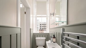 Un baño pequeño con inodoro, lavamanos y una ventana sobre el lavamanos.
