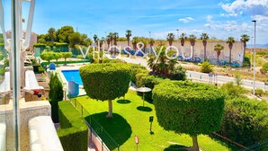 A landscaped area with a swimming pool, neatly trimmed hedges, and a road with palm trees. - Torrevista La Mata Penthouse by Villas&You (Torrevieja)