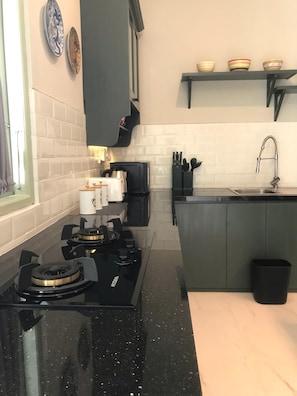 Una cocina con estufa a gas, cafetera, pileta y una pequeña isla con un bote de basura.