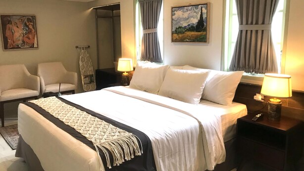 Een hotelkamer met een bed, twee stoelen, een bureau, een lamp, een schilderij en een raam met gordijnen.