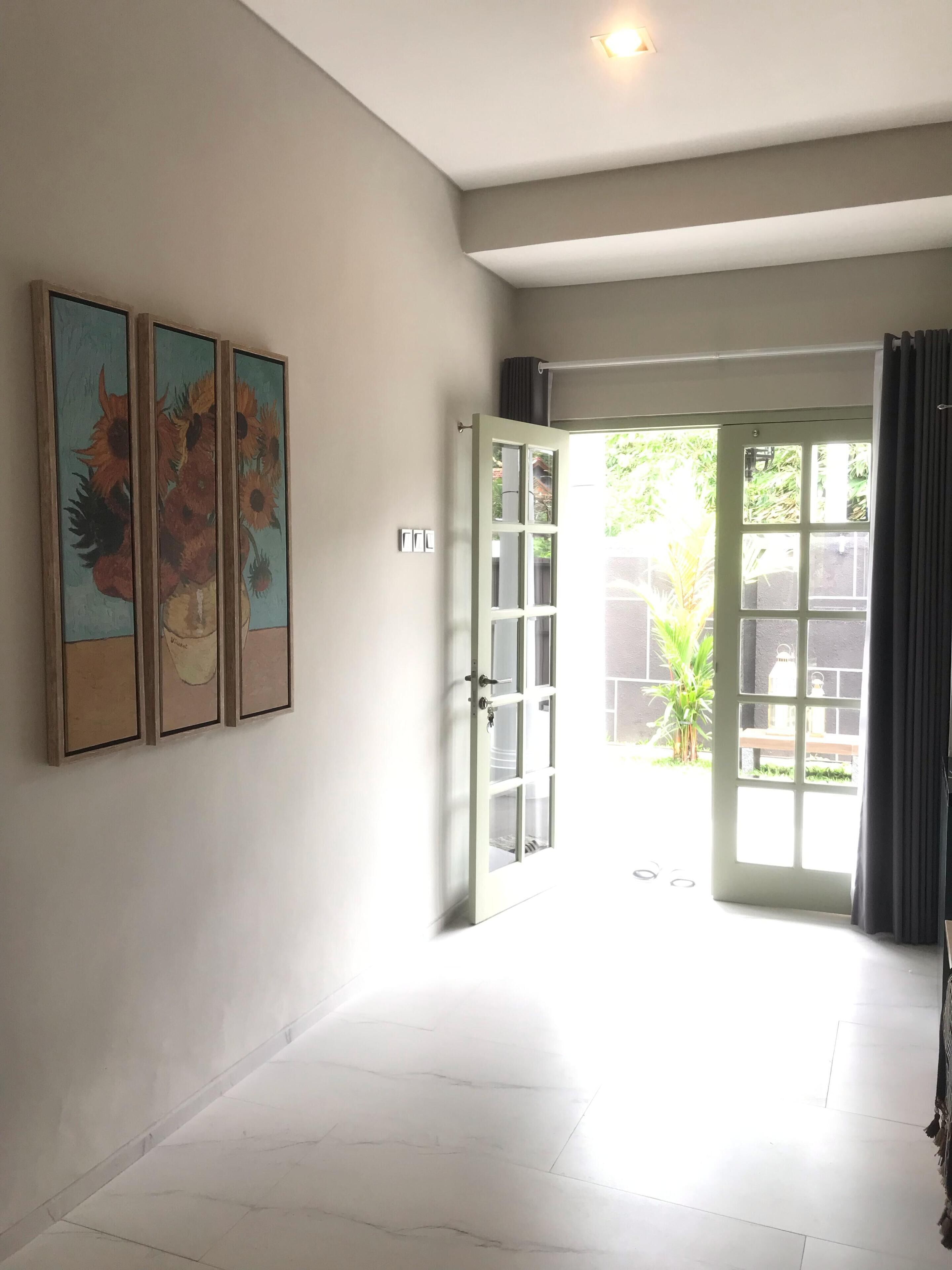 Un pasillo con una puerta que da a un jardín, un cuadro colgado en la pared y una lámpara en el techo.