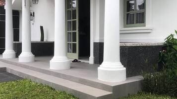 A building with a covered porch supported by white columns, a stone pathway leading to the entrance, and a small garden area with grass and pebbles.