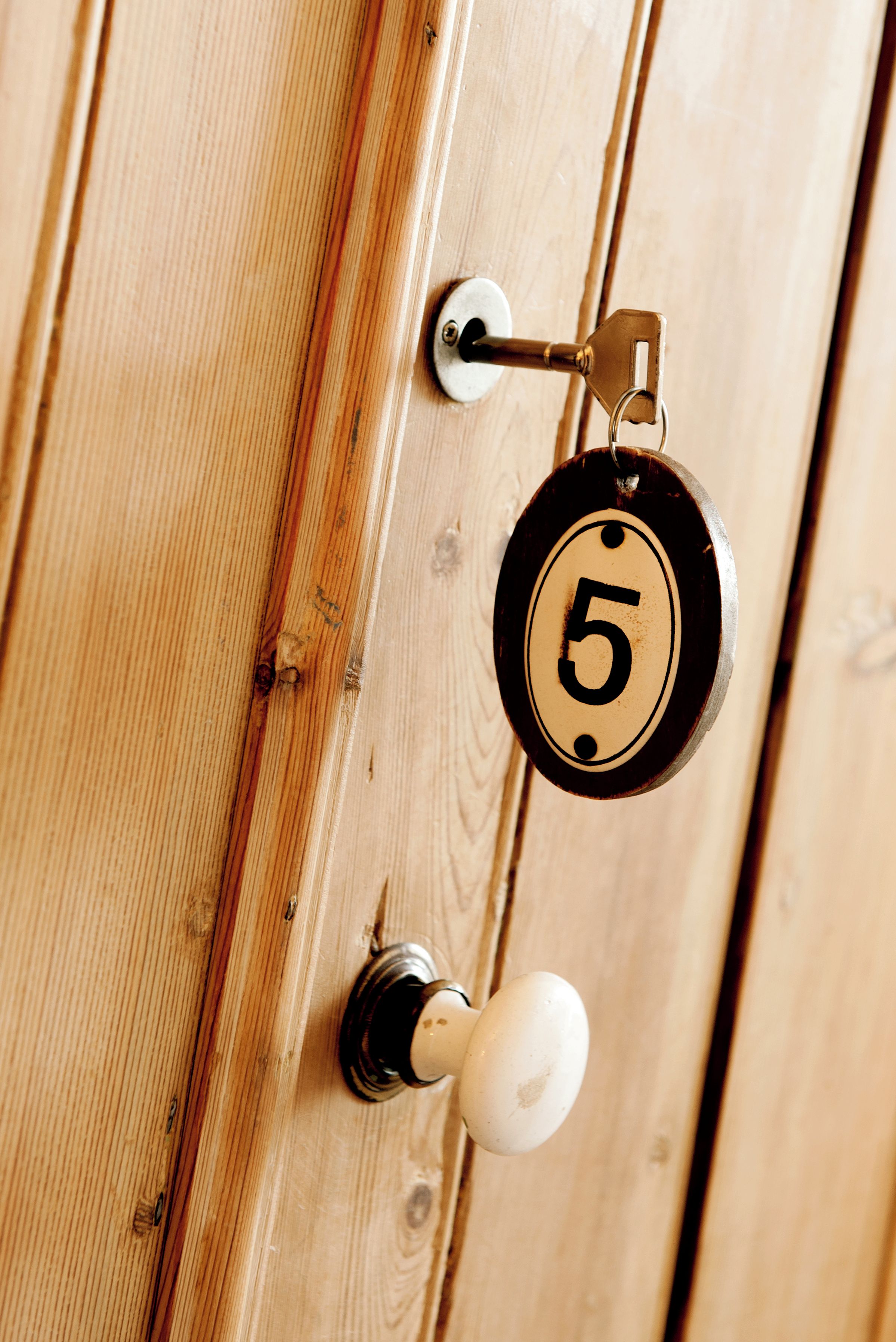 A wooden door with a brass doorbell and a round, numbered plaque.