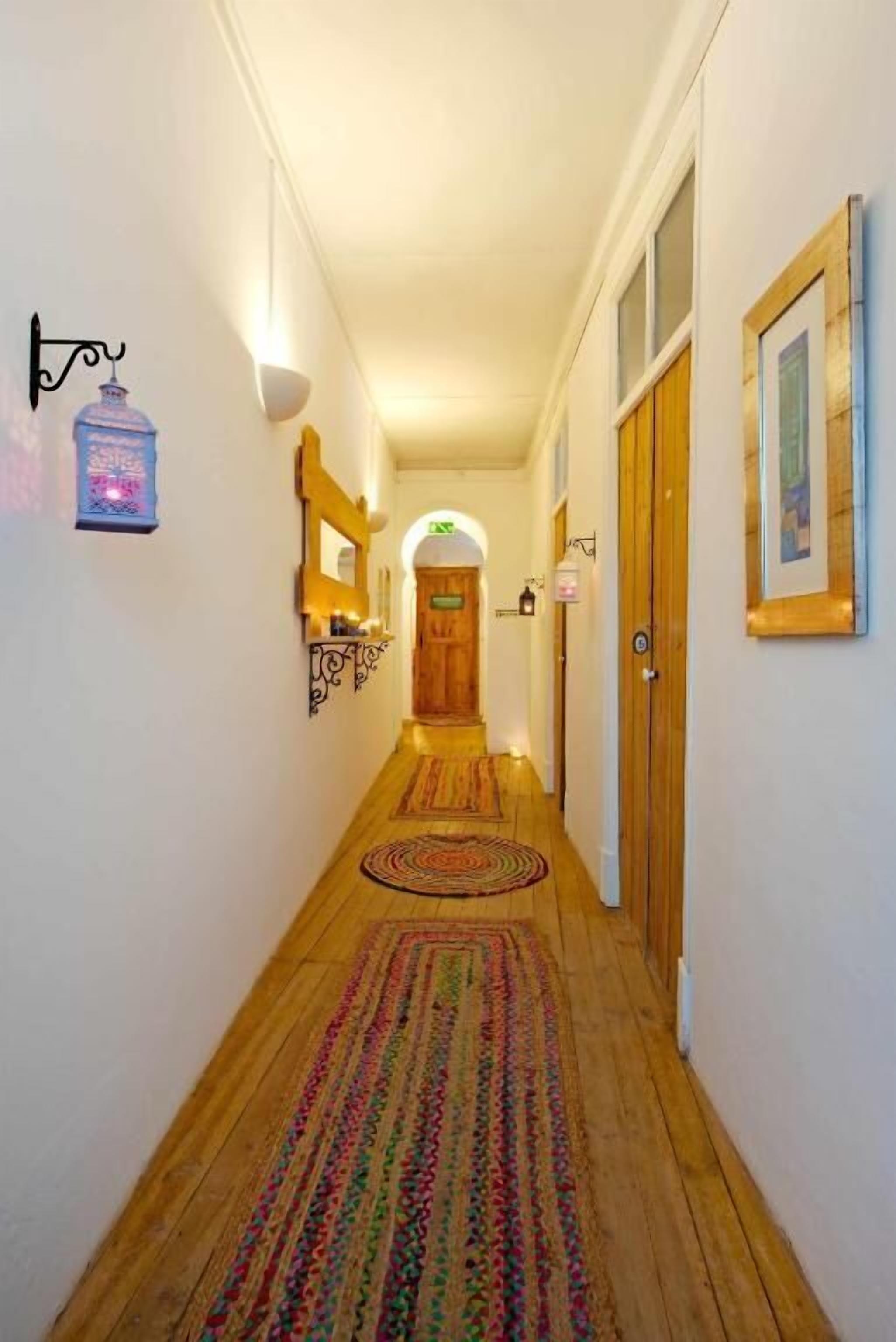 Un couloir étroit doté d’un plancher en bois, d’un tapis à motifs, d’une porte en bois et d’un luminaire fixé au mur.