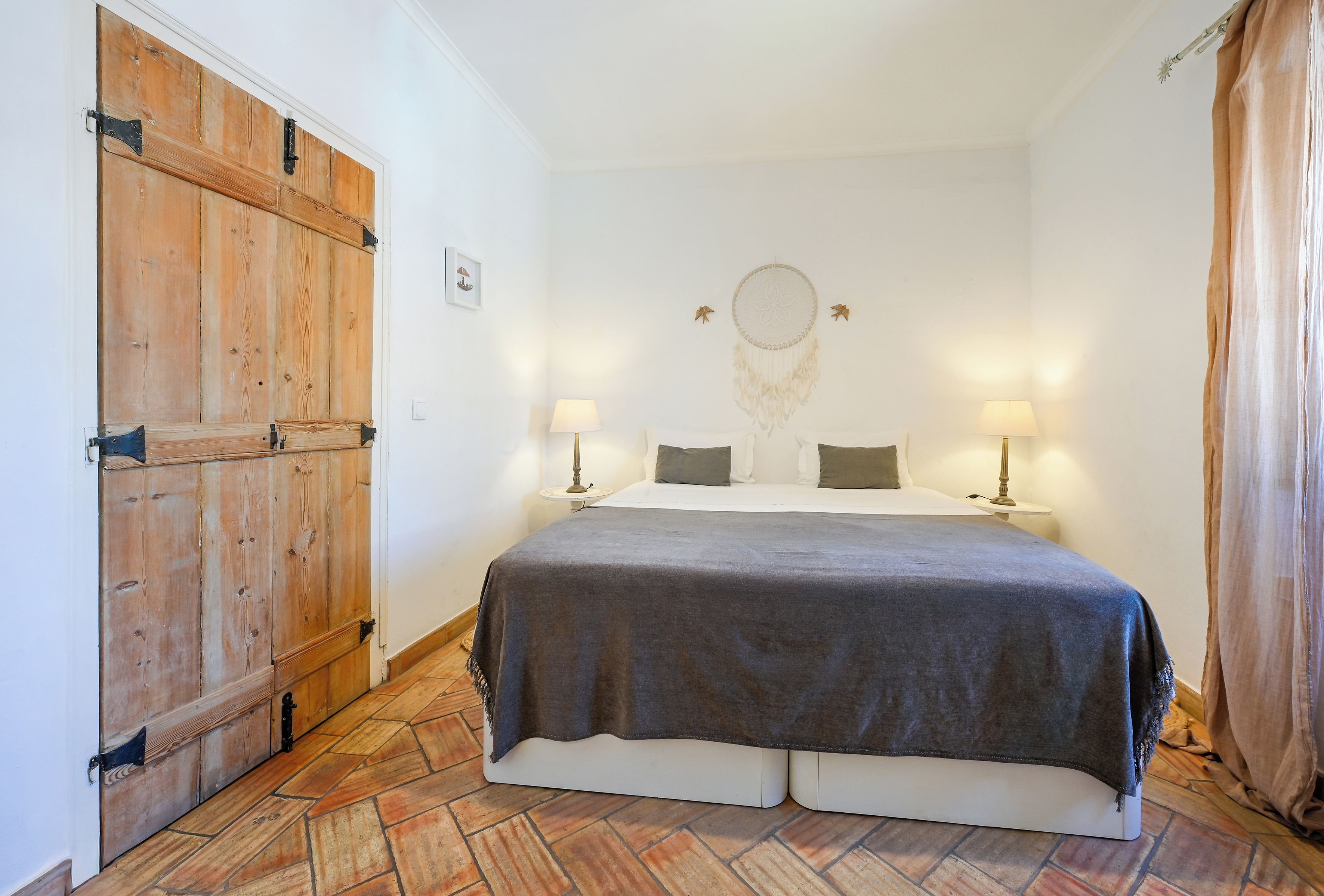Quarto com uma cama grande, duas luminárias de cabeceira, um sonho apanhado na parede e um guarda-roupa de madeira.