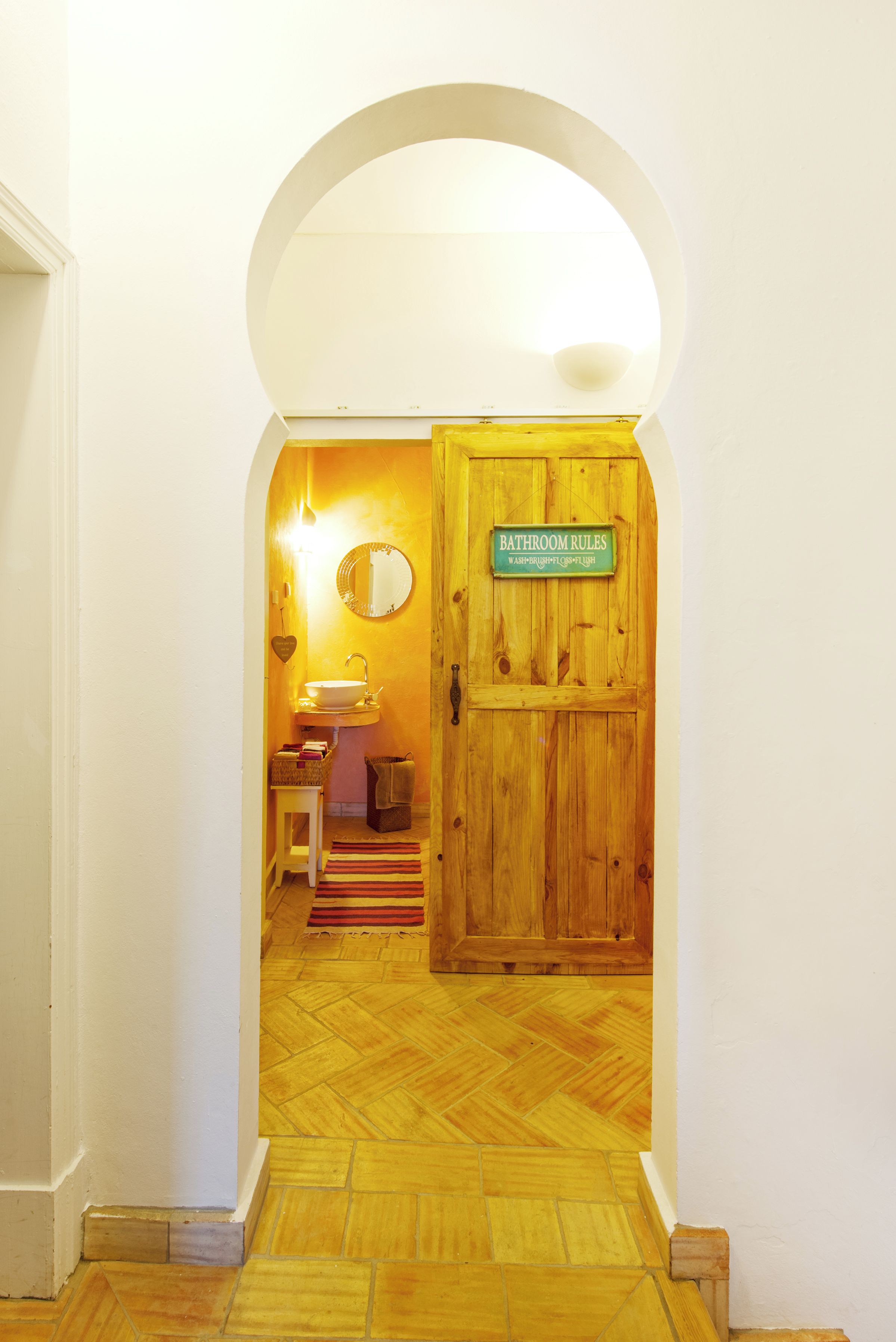 Un pasillo que conduce a un baño con puerta de madera, lavamanos y espejo.
