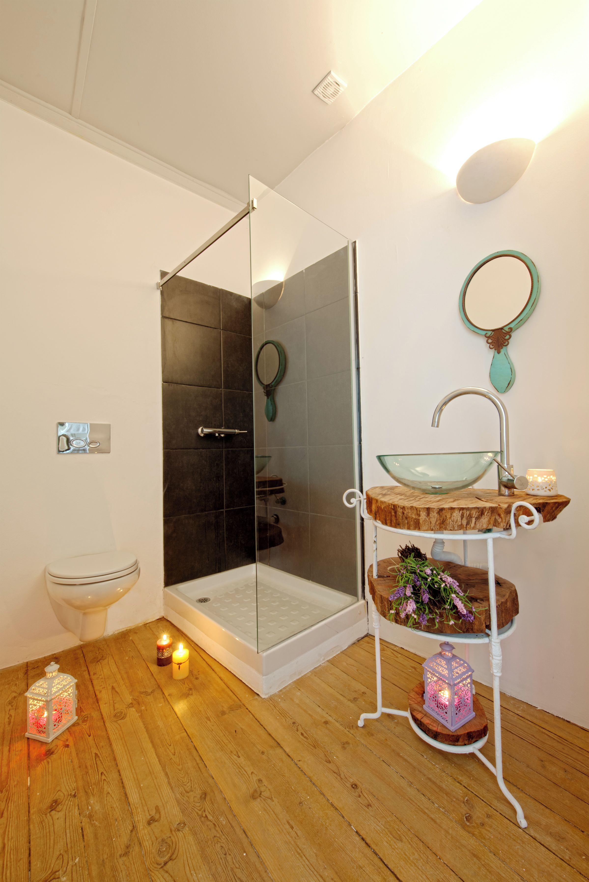A modern bathroom with a glass shower enclosure, a white sink with a glass bowl, and a wooden shelf with decorative items.