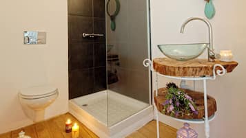 A modern bathroom with a glass shower enclosure, a white sink with a glass bowl, and a wooden shelf with decorative items.