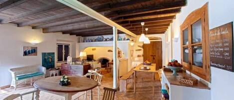 A rustic interior with a wooden ceiling, a round table with chairs, a sofa, and a chalkboard menu.