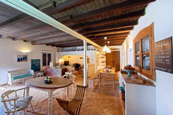 A rustic interior with a wooden ceiling, a round table with chairs, a sofa, and a chalkboard menu.