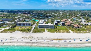 An aerial view of a coastal area with buildings, a beach, and turquoise waters. - Sanibel Surfside 234: Beautifully Updated with Gulf Views! 2 PB Courts! (Sanibel)