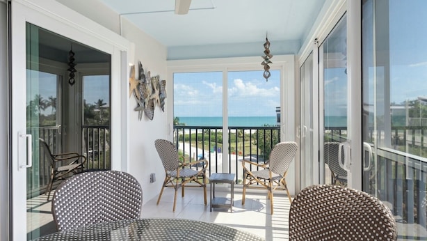 A balcony with wicker furniture, a ceiling fan, and a view of the ocean. - Sanibel Surfside 234: Beautifully Updated with Gulf Views! 2 PB Courts! (Sanibel)