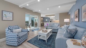 A modern living room with a sofa, armchair, and coffee table, a kitchen in the background, and a balcony with a view. - Sanibel Surfside 234: Beautifully Updated with Gulf Views! 2 PB Courts! (Sanibel)