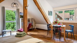 Un dormitorio con un ventanal grande, techo de madera, una cama, una mesita y una silla.