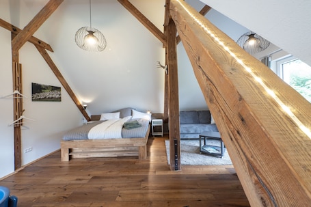 A bedroom with a sloped ceiling, wooden beams, a bed, a gray sofa, and pendant lights.. Room Köpfleblick with Mountain View and Wi-Fi