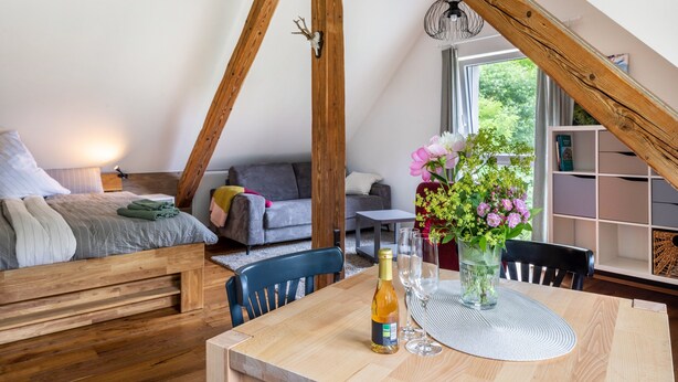 Un acogedor dormitorio tipo loft con techo de madera, una cama, una mesa de comedor con sillas y un ventanal con vistas a zonas verdes.